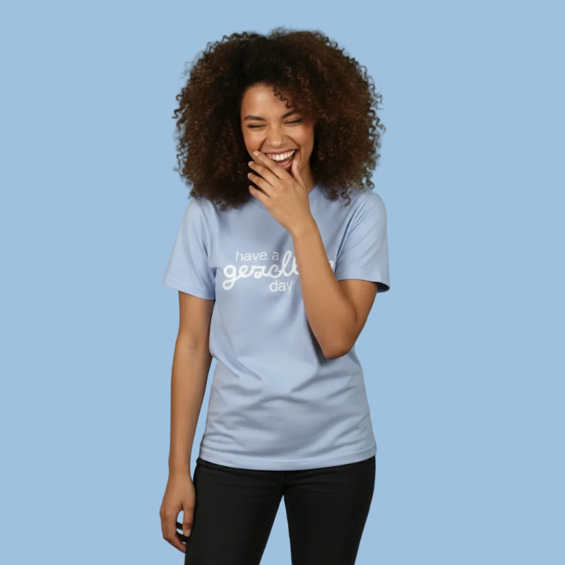 Woman wearing a light blue t-shirt with Have a Gezellige Day ptint, smiling against a plain background